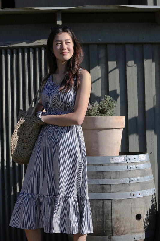 Melina wears the Martina Midnight navy pinstripe midi dress with a woven tote beside a terracotta lavender planter