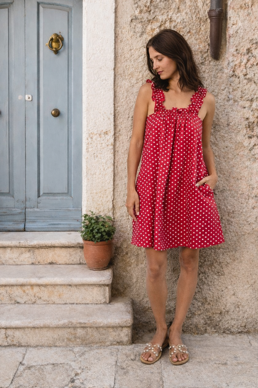 Woman in a red Mila polka dot dress standing against a stone wall with a blue door.
