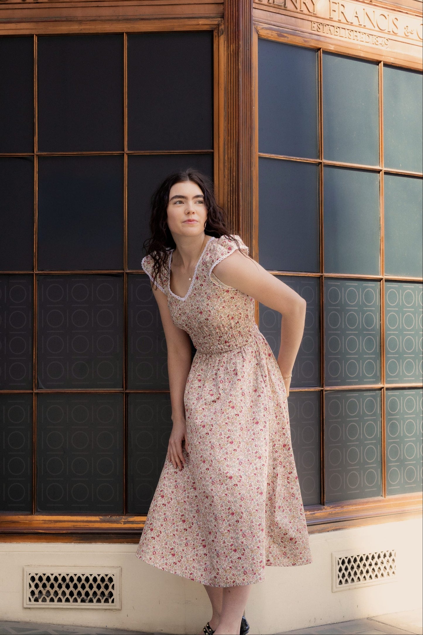 Juliet Wildflower floral cotton midi dress — full-length front view against vintage shopfront in warm afternoon light