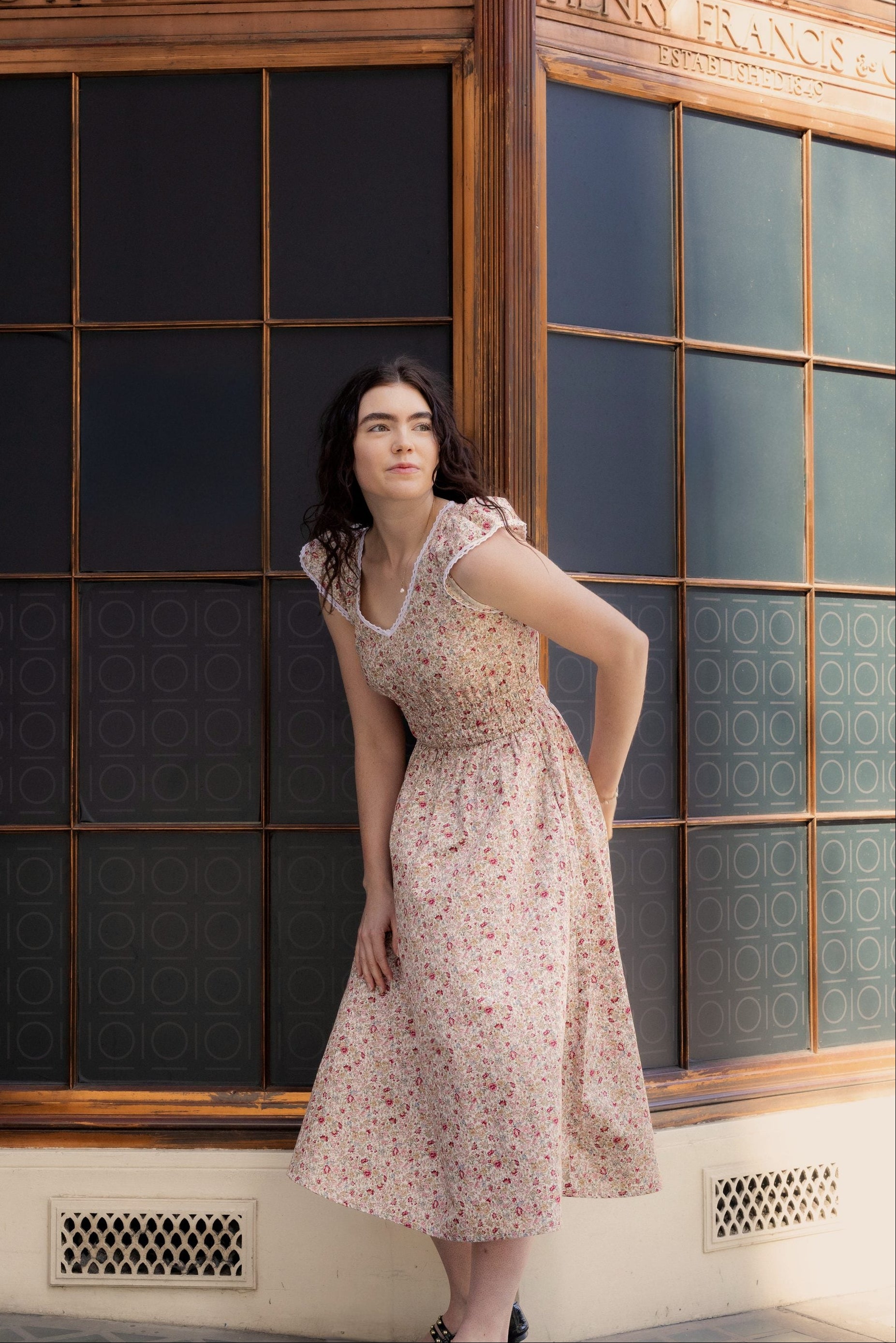 Juliet Wildflower floral cotton midi dress — full-length front view against vintage shopfront in warm afternoon light